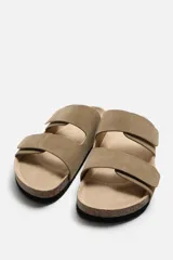 Sandalias color beige de piel con acabado serraje, doble tira con cierre adherente y plantilla anatómica.