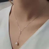 Collar estilo 'Y' o 'Lariat' con cadena de plata 925, un punto de unión con una circonia engarzada y un colgante final de perla de río de forma ovalada.