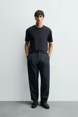 Pantalón de denim azul oscuro, corte wide fit, largo cropped, con pliegues frontales, bolsillos laterales y traseros asimétricos. Cierre frontal con cremallera y gancho metálico oculto.
