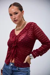 Blusa de manga larga color bordó, con tejido de punto calado, escote en V con volados y cierre frontal anudado.