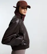 Campera bomber femenina de cuero sintético color marrón oscuro, con cuello alto, frisos en los hombros, puños y bajo ajustados, y cierre delantero con cremallera.