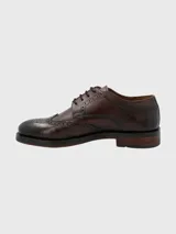 Zapato de vestir marrón oscuro con cordones, estilo Oxford, con detalles de perforaciones y costuras en cuero.