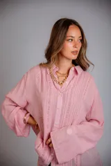 Camisa color beige claro, de corte holgado, con cuello clásico, cierre frontal con botones, mangas largas con puños abotonados y detalles de broderie en la parte delantera.