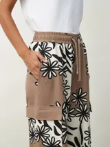 Pantalón de tela color marrón con estampado de flores blancas y negras, de corte palazzo con bolsillos laterales y cintura con cordón.