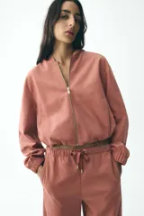 Chaqueta corta color rosa con capucha y manga larga terminada en puño. Tiene bolsillos de vivo en el delantero, bajo ajustable con cordones elásticos y cierre frontal con cremallera.