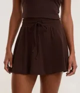 Short pollera color marrón de malla de algodón con cintura elástica y lazo ajustable. Prenda con buenas prácticas ambientales.