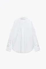 Camisa celeste de popelina de algodón, con cuello solapa, escote pico, manga larga con puños y cierre frontal con botones.