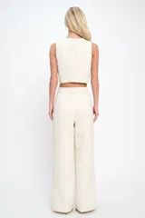 Conjunto de chaleco y pantalón color crema con textura tweed. El chaleco es sin mangas, con escote en V y cierre frontal con botones dorados. El pantalón es de corte recto con bolsillos laterales.