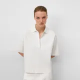 Polo de mujer color crudo, confeccionado en punto cerrojillo. Presenta cuello con solapa y escote en pico, y mangas cortas.