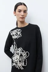 Sweater color rosado melange con cuello redondo y manga larga. Presenta un bordado abstracto en color crema en la parte frontal.