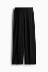 Pantalón sastrero negro de tejido suave con cintura elástica de tiro alto, cierre y pretina prolongada con botón. Modelo con bolsillos al bies, solapa decorativa con botón adelante y bolsillos de atrás insertados. Piernas amplias con pinzas y pliegues adelante y atrás.
