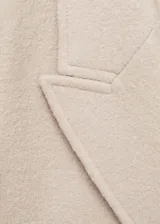 Abrigo largo color beige de lana virgen con doble botonadura, cuello con solapa ancha, hombros marcados y abertura en la parte posterior del bajo.