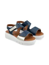 Sandalia con plataforma blanca, base marrón y tiras de cuero metalizado azul marino y plateado, con ajuste de velcro en el tobillo y el empeine.
