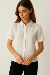 Camisa blanca de algodón con bordado tipo broderie, corte clásico, cuello camisero, manga corta con dobladillo y cierre frontal con botones.