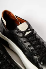 Zapatillas urbanas de cuero negro con cordones, suela blanca y detalles en marrón.