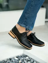 Zapato acordonado de cuero vacuno color marrón oscuro, con suela de goma, horma cuadrada y tacón bajo.