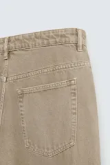 Pantalón de denim color beige, corte relaxed fit, con bolsillos laterales tipo cargo con solapa y cierre de botón. Cierre frontal con botón y cremallera.