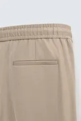 Pantalón color topo de corte recto, con cintura elástica ajustable con cordón, bolsillos laterales y bolsillos de vivo en la espalda.
