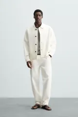 Pantalón de jean color blanco, corte recto, con bolsillos frontales y traseros, y cierre frontal con cremallera y botón.