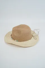 Sombrero de paja de ala ancha, con copa estilo fedora en color marrón y ala en color beige claro con hilos dorados entretejidos. Presenta una cinta decorativa con cuentas turquesas y un lazo de cordón fino atado alrededor de la base de la copa.
