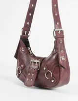 Cartera de hombro de cuero vegano color marrón con acabado texturizado. Presenta un diseño estilo hobo con hebilla frontal decorativa, herrajes metálicos plateados, argollas laterales y correa ajustable.