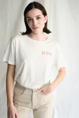 Remera de manga corta color blanco roto, con cuello redondo y un pequeño estampado frontal del logo de la banda Def Leppard en color rosado.
