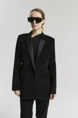 Saco negro de corte oversize con solapas de satén contrastantes, hombros marcados y cierre frontal de un solo botón.