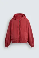 Cazadora relaxed fit color ladrillo confeccionada en tejido de algodón con estructura canvas. Tiene cuello con capucha ajustable, manga larga, bolsillos frontales de vivo, acabados con rib elástico, efecto lavado y cierre frontal de cremallera.