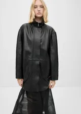 Abrigo negro oversize de cuero ovino con cuello alto y cierre frontal con cremallera y botones ocultos.