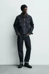 Bota corta de piel negra, estilo motociclista, con caña media y punta cuadrada. Presenta una correa ajustable con hebilla metálica en el tobillo y otra en la parte superior de la caña.