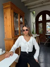 Blusa blanca crop con escote en V y volados, mangas largas acampanadas.