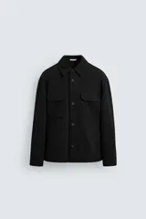 Sobrecamisa negra de corte relaxed fit, con cuello solapa, manga larga con puños abotonados, bolsillos de plastrón con solapa en el pecho y bolsillos de vivo en la cadera. Cierre frontal con botonadura.