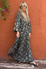 Vestido largo de manga larga, con escote en V y estampado floral en tonos negro, beige y gris. Presenta un detalle de borde estampado en la parte inferior de la falda.