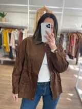 Chaqueta marrón de símil gamuza con cuello de cuerina, cierre frontal, bolsillos con solapa y elástico ajustable en la cintura.