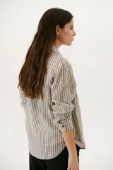 Camisa a rayas verticales color beige y blanco, con cuello clásico, botones marrones y mangas largas.
