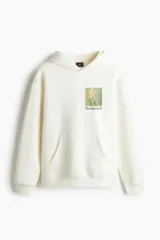 Buzo canguro color crema con capucha cruzada de doble capa, hombros caídos, bolsillo tipo canguro, puños y bajo acanalados. Estampado frontal con flores y texto "Beautanical". Corte holgado.