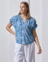 Blusa celeste estampada con motivos de playa, con cuello a la base y escote en V. Mangas cortas con detalle fruncido.
