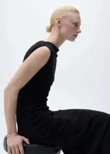 Vestido midi negro de corte ajustado, con cuello asimétrico y sin mangas. Presenta cintura drapeada y largo midi.