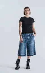 Bermuda larga de denim azul con lavado ácido y efecto desgastado. Presenta un calce oversize, talle alto con cinturón de tela a juego y ruedos deshilachados.