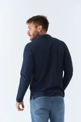 Polo de manga larga negra con cuello clásico, tapeta de dos botones y bolsillo de parche en el pecho con ribete blanco. Logo de la marca bordado en blanco sobre el bolsillo.