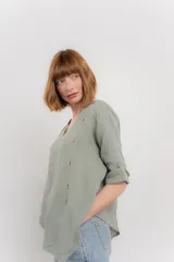 Blusa color naranja confeccionada en 100% lino, con escote en V, mangas cortas con vuelta y silueta amplia. Presenta terminación asimétrica y fila de botones decorativos en uno de los hombros.