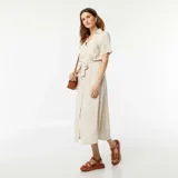 Vestido largo color beige, estilo camisero, con cuello clásico, mangas cortas, abotonadura frontal y lazo en la cintura.