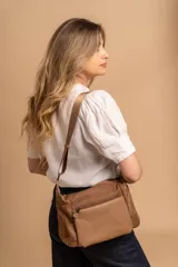 Bandolera de diseño moderno, color beige rosado, con correa regulable y bolsillo frontal con cierre.