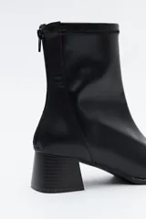 Bota corta de caña elástica color negro, con puntera cuadrada y taco geométrico de altura media. Presenta cierre de cremallera en la parte trasera.