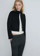 Chaqueta corta negra con cuello mao, cierre frontal con cremallera, dos bolsillos laterales y un bolsillo de ribete en el pecho.