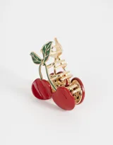 Broche para el pelo dorado con forma de cerezas rojas y hojas verdes.
