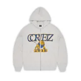 Campera con capucha gris jaspeado, con cierre frontal y cordones ajustables. Estampado frontal con el logo de Corteiz, un león y el número 2018 en azul y amarillo.