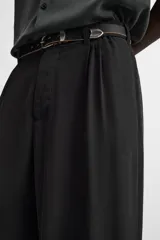 Pantalón negro de corte amplio confeccionado en tejido con mezcla de viscosa. Presenta cintura elástica, pliegues en la parte delantera, bolsillos laterales y traseros de vivo. Cierre frontal con cremallera y gancho metálico oculto.