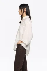 Camisa blanca de corte ancho y silueta relajada, con cuello camisero, botones frontales, manga 3/4 ancha con puño y bolsillo de plastrón en el pecho.