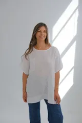 Blusa blanca de lino con cuello redondo, mangas cortas, bolsillo en el pecho y detalle de bordado calado en el lateral inferior. Corte holgado.